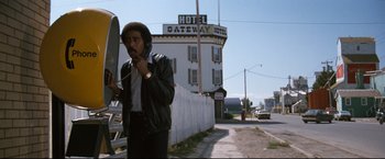 Movie still from “Superman III” (1983), directed by Richard Lester – A man talking on a phone while standing in front of a hotel; Medium shot, Low angle