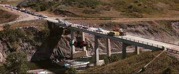 Movie still from “Superman III” (1983), directed by Richard Lester – A man flying through the air while riding a skateboard over a bridge; Extreme Wide shot, High angle