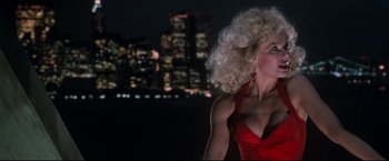 Movie still from “Superman III” (1983), directed by Richard Lester – A woman in a red dress is standing in front of a city skyline at night; Medium shot, Low angle