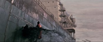 Movie still from “Superman III” (1983), directed by Richard Lester – A person standing on a ledge near a building; Extreme Wide shot, Low angle