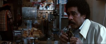 Movie still from “Superman III” (1983), directed by Richard Lester – A man sitting at a table eating a hot dog; Close Up shot, High angle