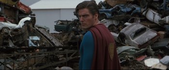 Movie still from “Superman III” (1983), directed by Richard Lester – A man wearing a superman costume standing in a pile of junk; Medium shot, Over the shoulder angle