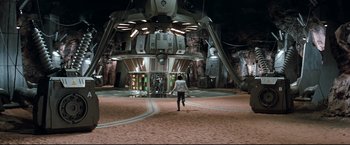 Movie still from “Superman III” (1983), directed by Richard Lester – A person walking in a room with a large metal structure; Extreme Wide shot, High angle