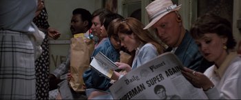 Movie still from “Superman III” (1983), directed by Richard Lester – A group of people standing around each other reading newspapers; Medium shot, Over the shoulder angle