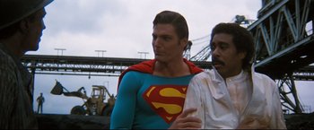 Movie still from “Superman III” (1983), directed by Richard Lester – A man in a superman costume standing next to another man; Medium shot, Over the shoulder angle