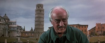 Movie still from “Superman III” (1983), directed by Richard Lester – An old man with a beard and mustache in front of the leaning tower of pisa; Close Up shot, Low angle
