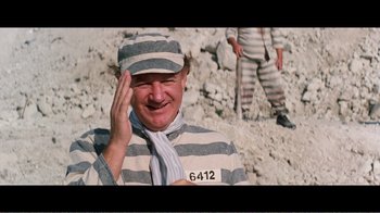 Movie still from “Superman IV: The Quest for Peace” (1987), directed by Sidney J. Furie – A man in a prison uniform is smiling for the camera; Medium shot, High angle