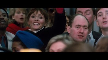 Movie still from “Superman IV: The Quest for Peace” (1987), directed by Sidney J. Furie – A crowd of people in a crowd with one person holding up a red object; Medium shot, Over the shoulder angle