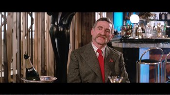 Movie still from “Superman IV: The Quest for Peace” (1987), directed by Sidney J. Furie – A man wearing a suit and tie sitting at a table with a martini glass; Medium shot, Low angle
