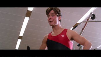 Movie still from “Superman IV: The Quest for Peace” (1987), directed by Sidney J. Furie – A young man in a red and black tank top is standing in a gym; Close Up shot, Over the shoulder angle
