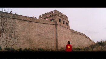 Movie still from “Superman IV: The Quest for Peace” (1987), directed by Sidney J. Furie – A man in a superman costume sitting on top of a brick wall; Extreme Wide shot, Low angle