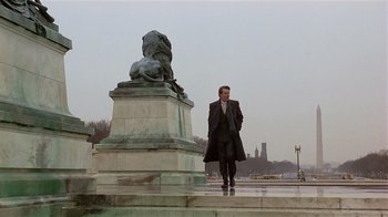 Movie still from “Suspect” (1987), directed by Peter Yates – A man in a suit standing next to a statue of a lion; Wide shot, Low angle
