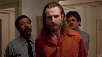 Movie still from “Suspect” (1987), directed by Peter Yates – A man with long hair and a long beard is standing next to two other men; Close Up shot, Low angle