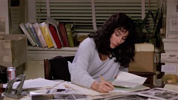 Movie still from “Suspect” (1987), directed by Peter Yates – A woman sitting at a desk writing on a piece of paper; Medium shot, High angle