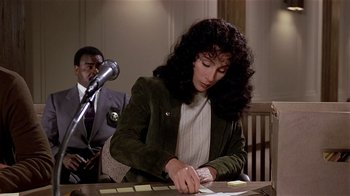 Movie still from “Suspect” (1987), directed by Peter Yates – A woman writing on a piece of paper in front of a microphone; Medium shot, Over the shoulder angle