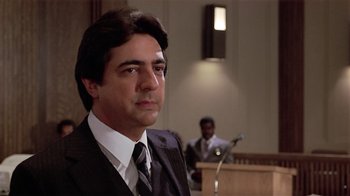 Movie still from “Suspect” (1987), directed by Peter Yates – A man wearing a suit and tie in front of a microphone; Close Up shot, Low angle