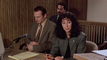 Movie still from “Suspect” (1987), directed by Peter Yates – A woman sitting at a table in front of two other people; Medium shot, High angle