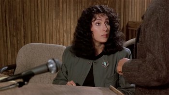 Movie still from “Suspect” (1987), directed by Peter Yates – A woman sitting at a table with a microphone in front of her; Close Up shot, Over the shoulder angle