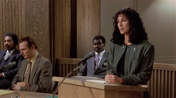 Movie still from “Suspect” (1987), directed by Peter Yates – A woman is speaking at a podium in a courtroom; Medium shot, High angle