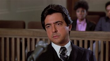 Movie still from “Suspect” (1987), directed by Peter Yates – A man in a suit and tie in front of a microphone in a courtroom; Close Up shot, Low angle