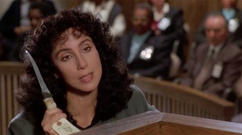 Movie still from “Suspect” (1987), directed by Peter Yates – A woman sitting at a table talking on the phone; Close Up shot, High angle