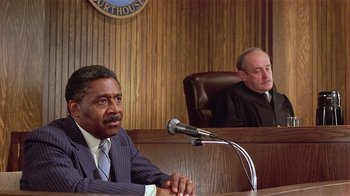 Movie still from “Suspect” (1987), directed by Peter Yates – Two men in suits sitting in front of microphones in a courtroom; Medium shot, Low angle