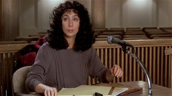 Movie still from “Suspect” (1987), directed by Peter Yates – A woman sitting in front of a microphone in a courtroom; Medium shot, Over the shoulder angle