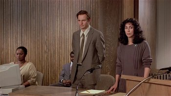 Movie still from “Suspect” (1987), directed by Peter Yates – A man and a woman standing in front of a microphone; Medium shot, Over the shoulder angle