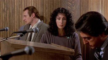 Movie still from “Suspect” (1987), directed by Peter Yates – A woman is sitting at a podium in front of a microphone; Medium shot, Over the shoulder angle