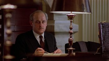 Movie still from “Suspect” (1987), directed by Peter Yates – A man sitting at a table in front of a lamp; Close Up shot, Low angle