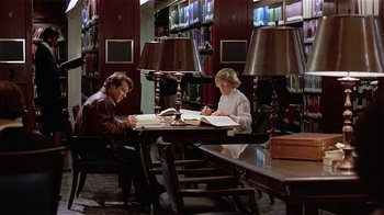Movie still from “Suspect” (1987), directed by Peter Yates – A man and a woman sitting at a table in a library; Wide shot, High angle