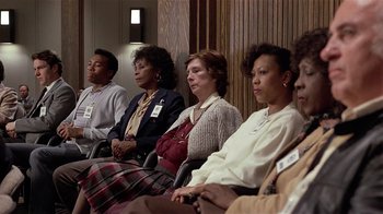 Movie still from “Suspect” (1987), directed by Peter Yates – A group of people sitting next to each other in a room; Medium shot, High angle