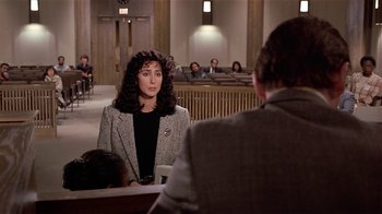 Movie still from “Suspect” (1987), directed by Peter Yates – A woman sitting in front of other people in a courtroom; Medium shot, Over the shoulder angle