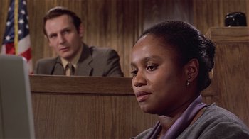 Movie still from “Suspect” (1987), directed by Peter Yates – A woman sitting in front of a man in a court room; Close Up shot, Over the shoulder angle