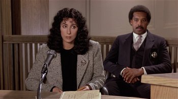Movie still from “Suspect” (1987), directed by Peter Yates – A woman sitting at a table in front of a microphone; Medium shot, High angle