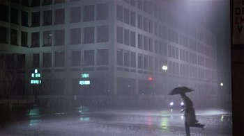 Movie still from “Suspect” (1987), directed by Peter Yates – A person holding an umbrella while standing in the rain; Extreme Wide shot, High angle