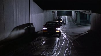 Movie still from “Suspect” (1987), directed by Peter Yates – A couple of cars driving down a street at night; Extreme Wide shot, High angle