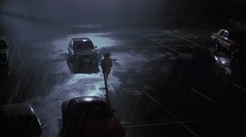 Movie still from “Suspect” (1987), directed by Peter Yates – A person walking in the rain next to a car; Extreme Wide shot, High angle