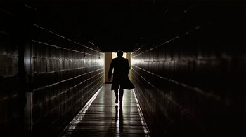 A man walking down a dark hallway holding a bag