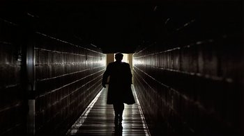 Movie still from “Suspect” (1987), directed by Peter Yates – A man walking down a dark hallway in a building; Wide shot, Low angle