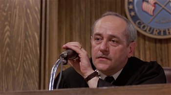 Movie still from “Suspect” (1987), directed by Peter Yates – An older man in a black robe and a black tie; Close Up shot, Low angle