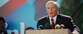 Movie still from “Swing Vote” (2008), directed by Joshua Michael Stern – An older man is speaking at a podium with microphones; Close Up shot, Low angle