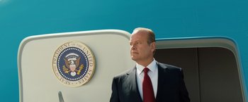 Movie still from “Swing Vote” (2008), directed by Joshua Michael Stern – A man in a suit and tie standing in front of a wall; Medium shot, Low angle