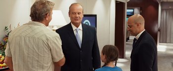 Movie still from “Swing Vote” (2008), directed by Joshua Michael Stern – A man in a suit and tie standing next to two other people; Medium shot, Over the shoulder angle