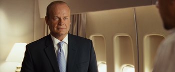 Movie still from “Swing Vote” (2008), directed by Joshua Michael Stern – A man in a suit and tie standing in front of an airplane window; Close Up shot, Low angle