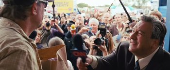 Movie still from “Swing Vote” (2008), directed by Joshua Michael Stern – A crowd of people gathered around a microphone in front of a camera; Medium shot, Over the shoulder angle