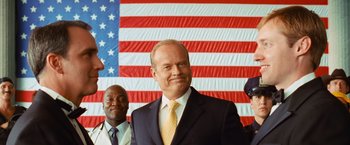 Movie still from “Swing Vote” (2008), directed by Joshua Michael Stern – A man in a suit and tie standing in front of an american flag; Medium shot, Low angle