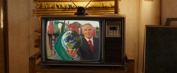 Movie still from “Swing Vote” (2008), directed by Joshua Michael Stern – A television with a picture of a man holding a globe in front of a playground; Medium shot, Low angle