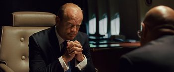 Movie still from “Swing Vote” (2008), directed by Joshua Michael Stern – A man in a black suit and white shirt sitting in front of a window; Close Up shot, Over the shoulder angle