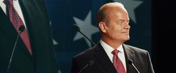 Movie still from “Swing Vote” (2008), directed by Joshua Michael Stern – A man in a black suit and a red tie standing in front of a microphone; Medium shot, Low angle